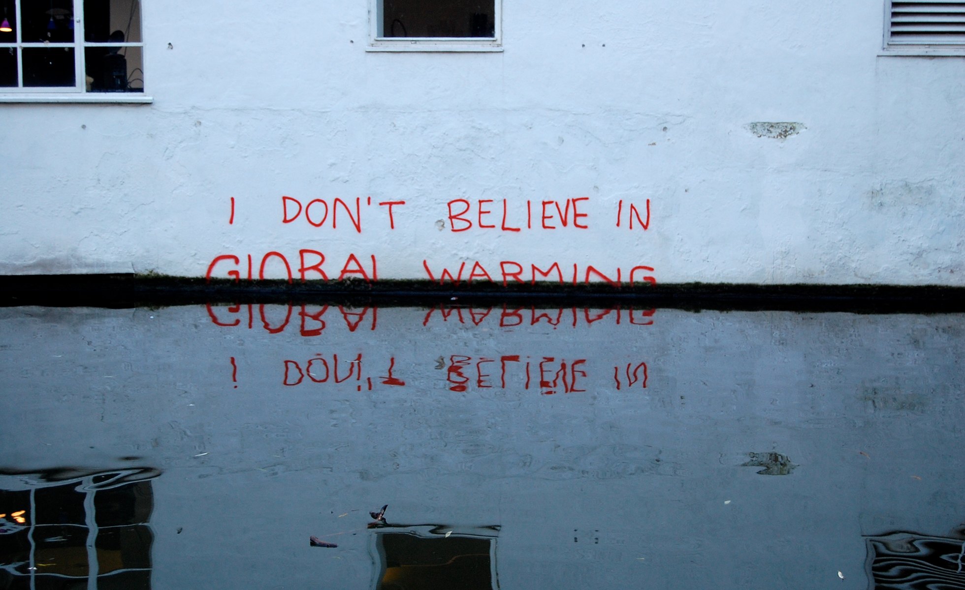 A graffiti tag stating "I don't believe in global warming" is immersed in rising water.