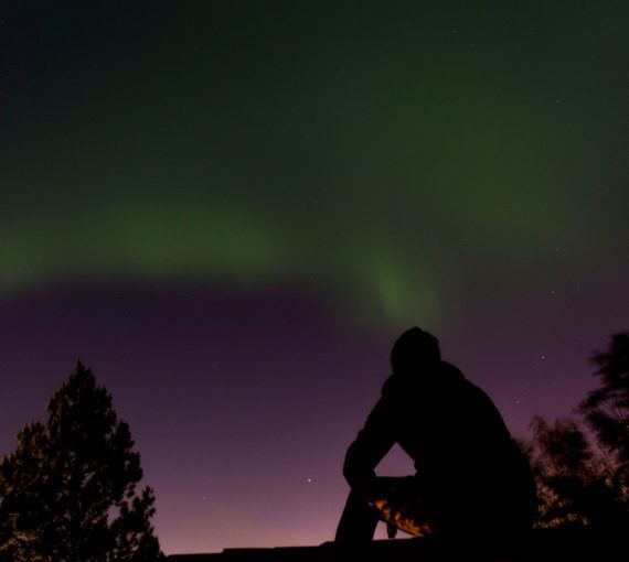 A person watches aurora illuminate the sky.