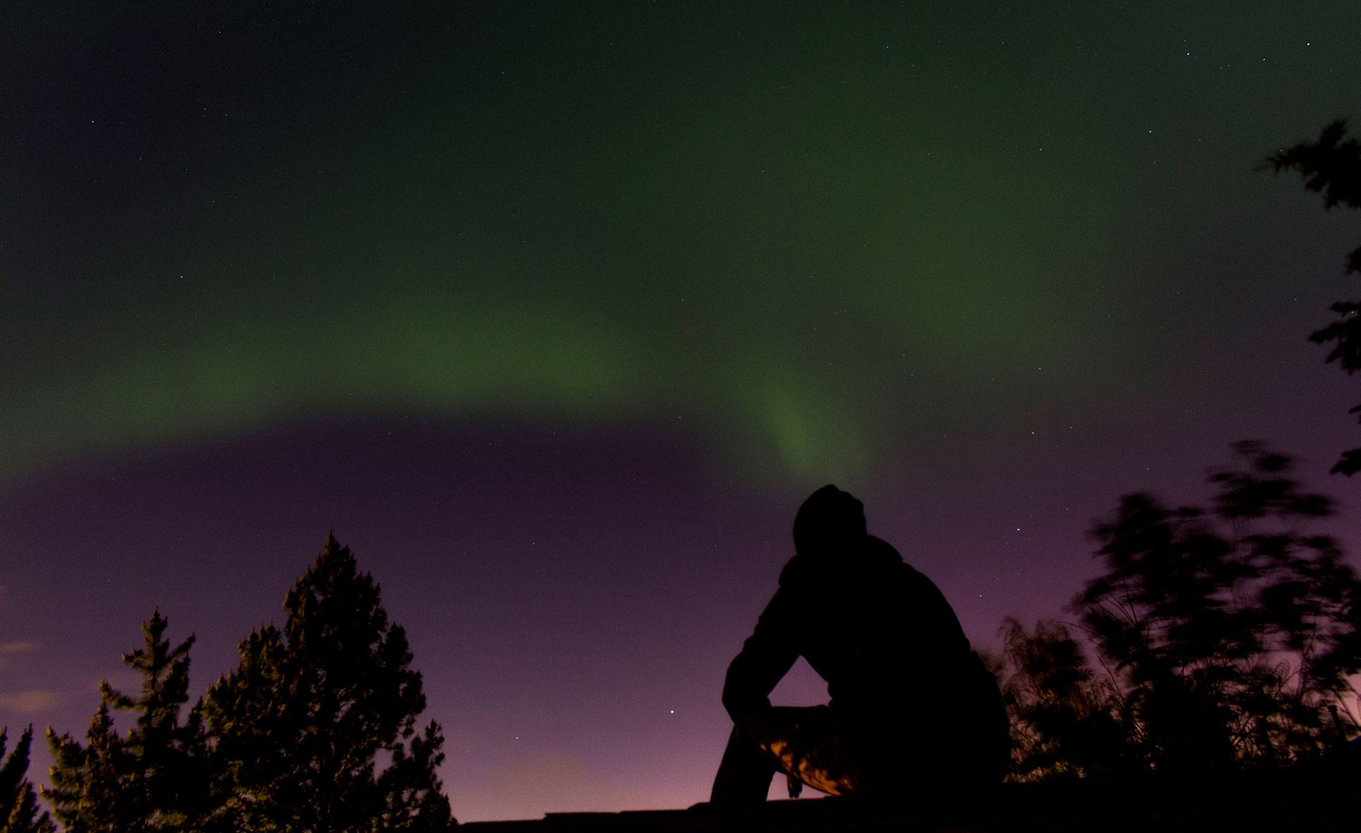 A person watches aurora illuminate the sky.