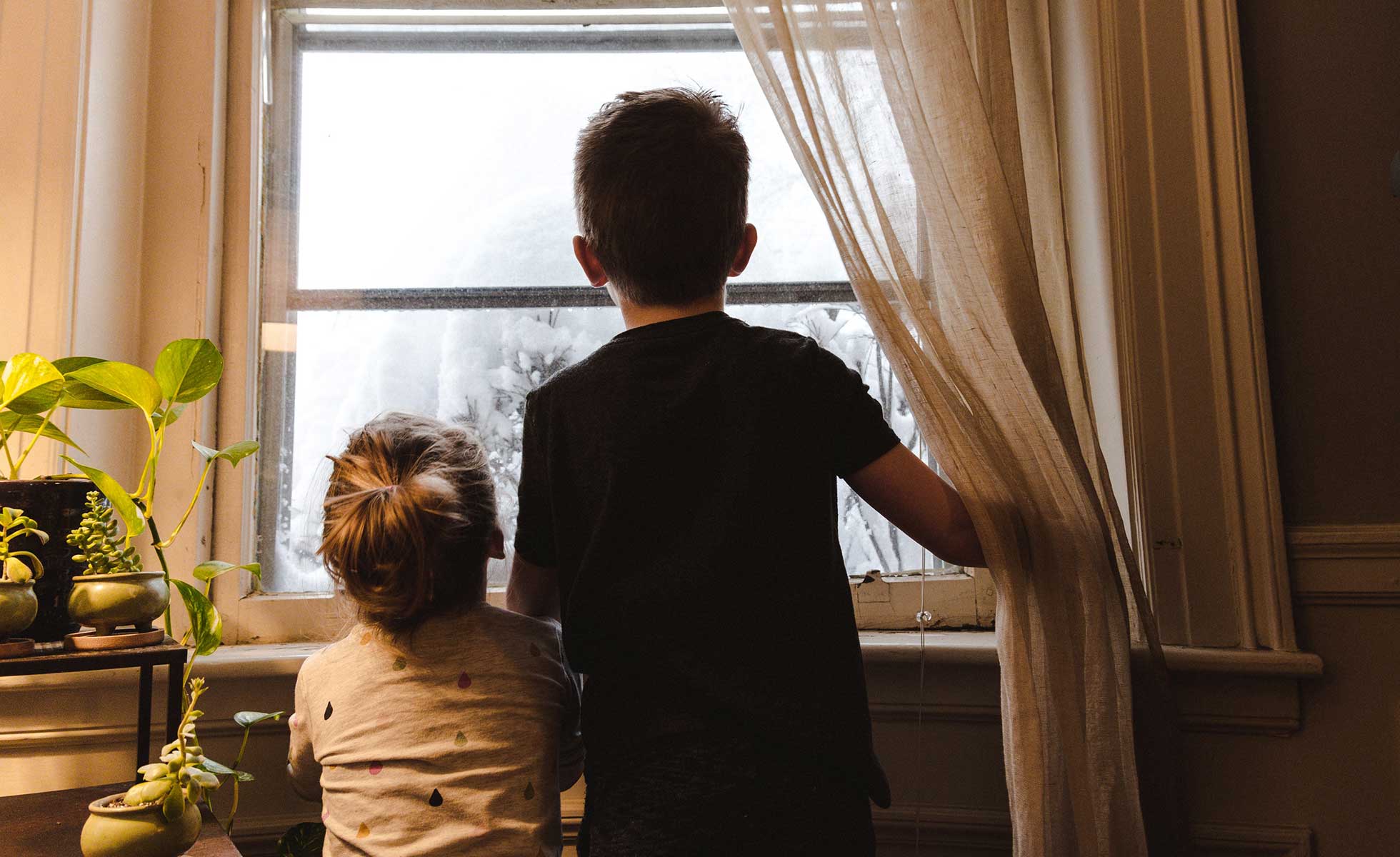 Children look out of a home window during winter