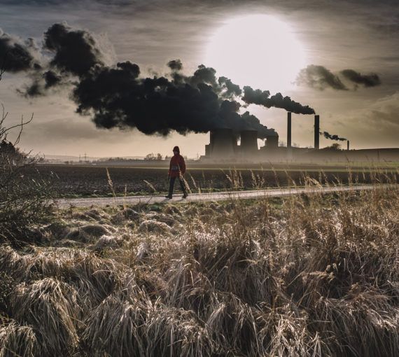 A person walks past polluting industrial activity in a rural area