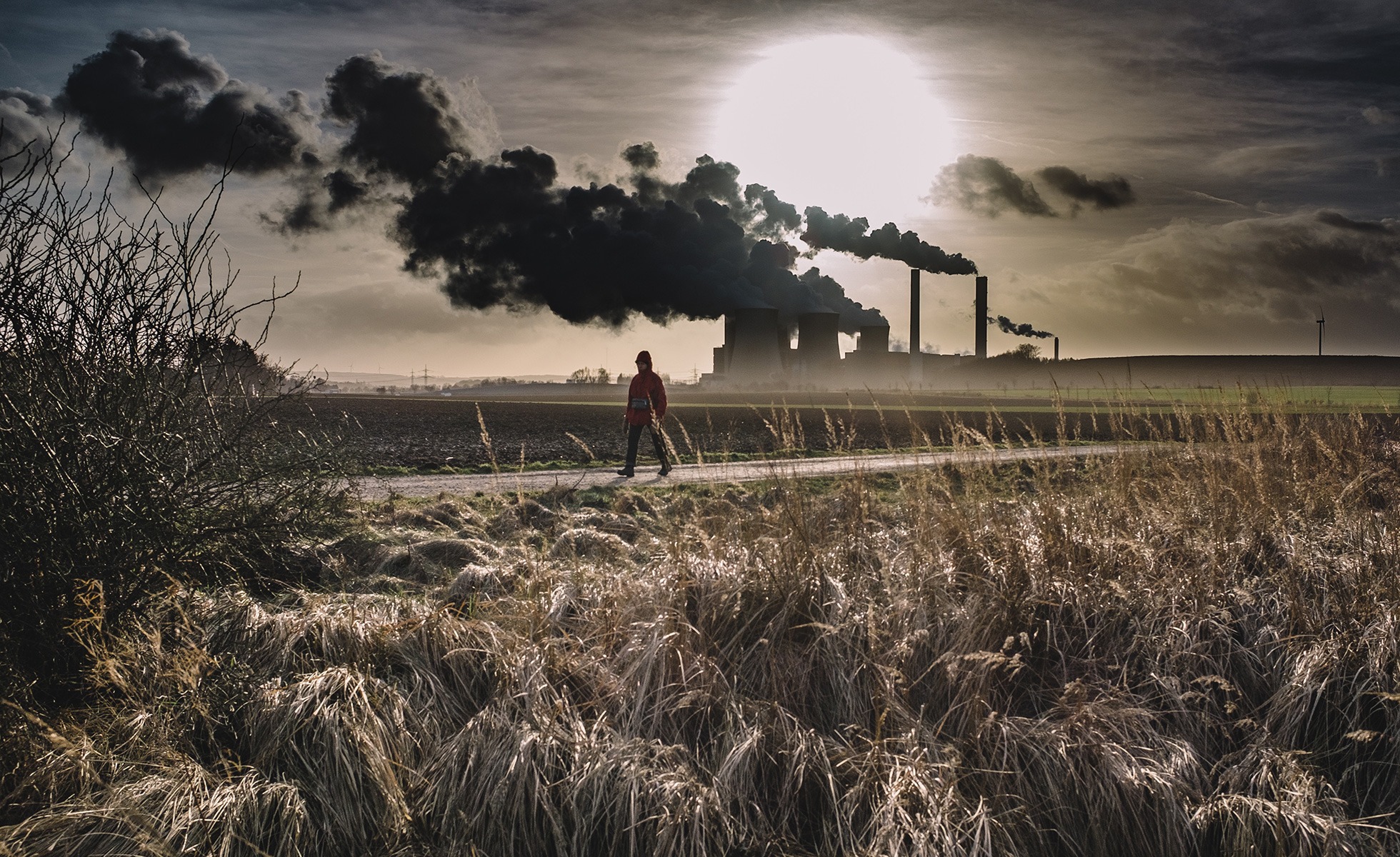 A person walks past polluting industrial activity in a rural area