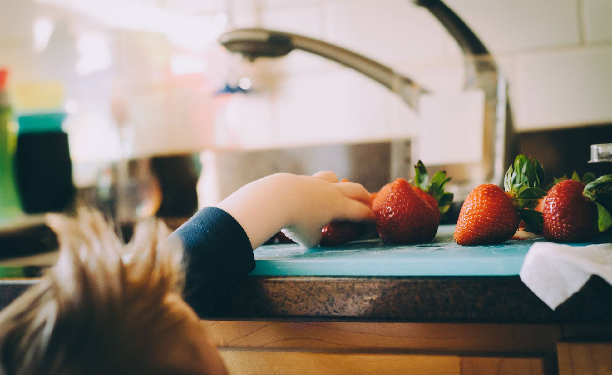 Child reaching for a washed strawberry
