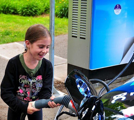 A young girl plugs in an electric vehicle to charge