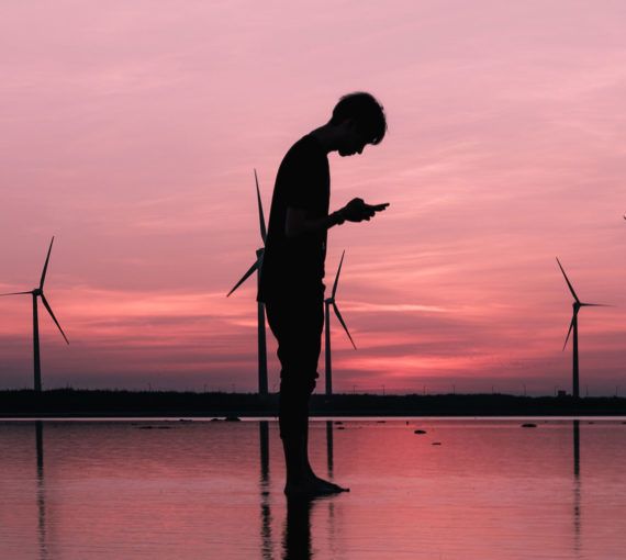 Young person reading online in front of wind turbines
