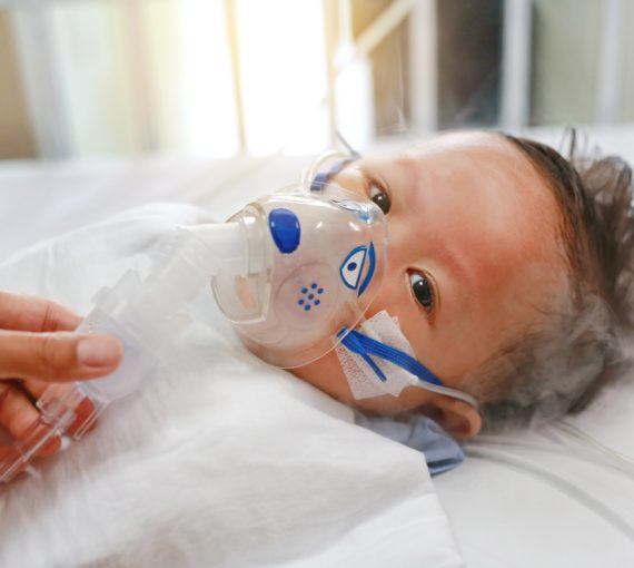 Sick baby boy applying inhale medication by inhalation mask to cure Respiratory Syncytial Virus (RSV) on patient bed at hospital.