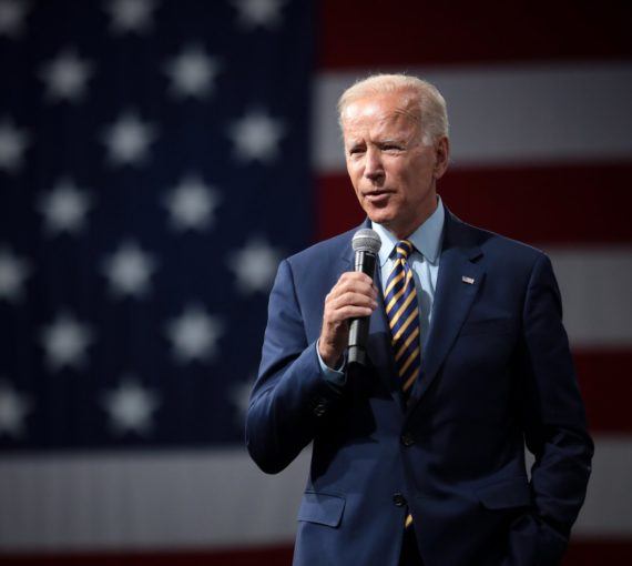 Joe Biden holding a microphone in front of USA flag