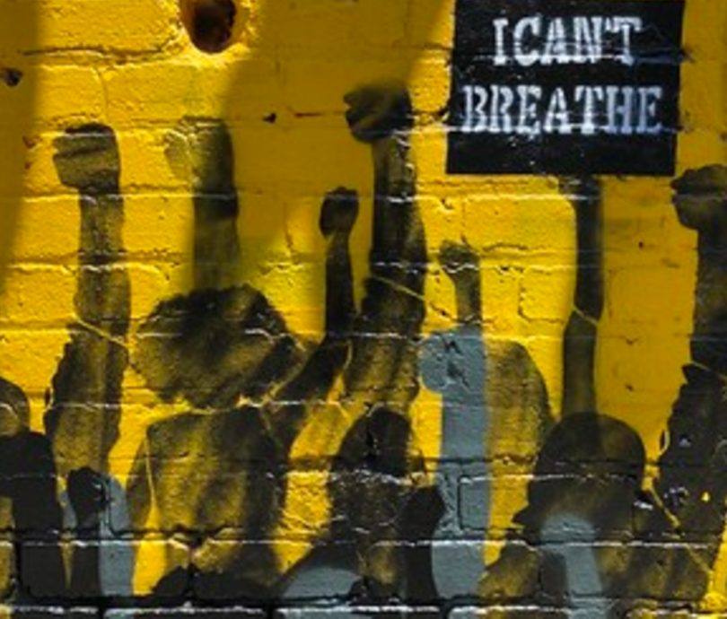 Mural of crowd with fists up holding I Can't Breathe sign against a yellow brick wall