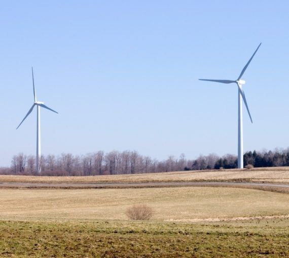 Two windmills in an open field under a blue sky