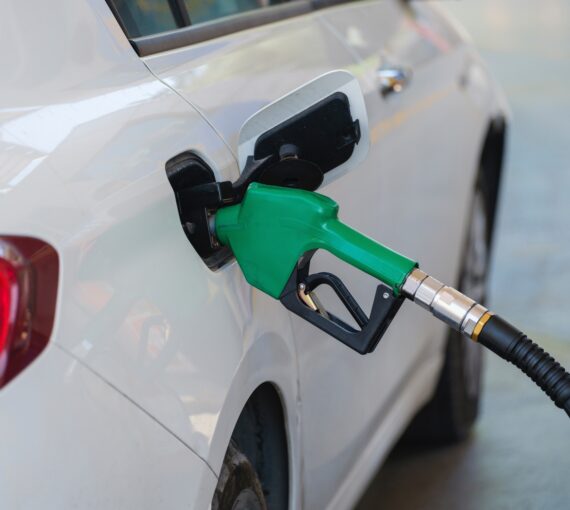 Green gas pump nozzle in the fuel tank of a white car