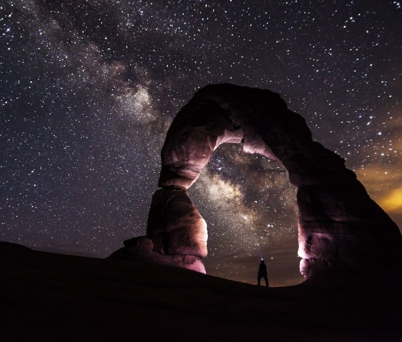 A person standing under a rock formation on a starry night