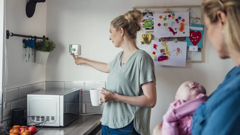 Woman in kitchen adjusting thermostat
