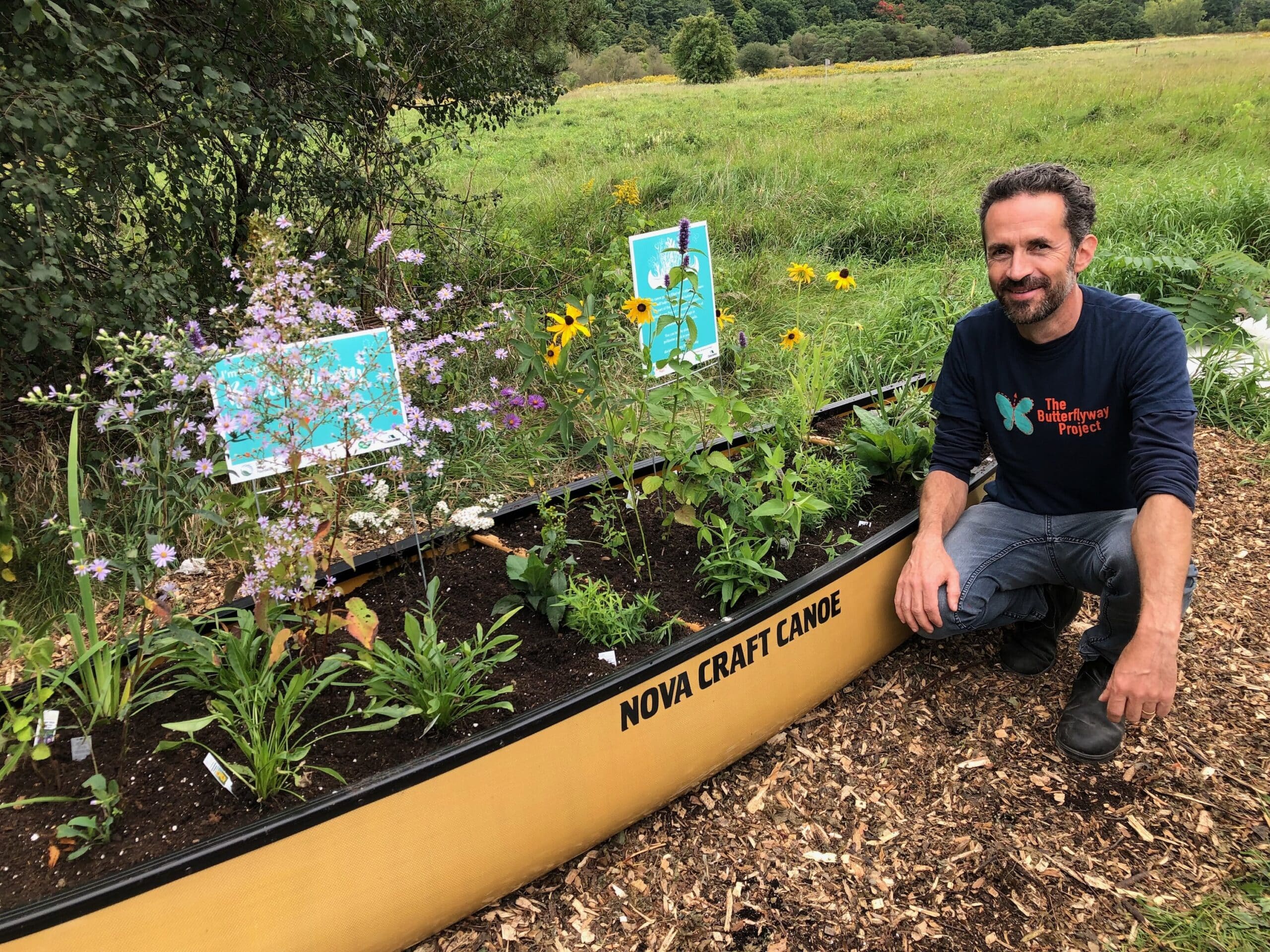 Man crouches in front of canoe filled with pollinator plants