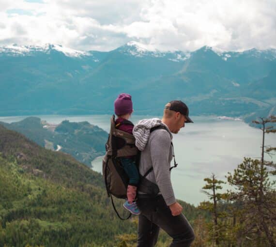 Man walks on top of mountain with a baby on his back