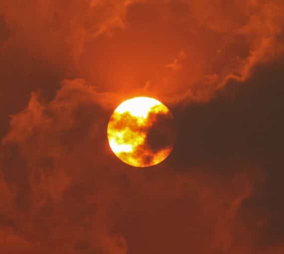A photo of an orange sun behind red clouds and smoke caused by forest fires.