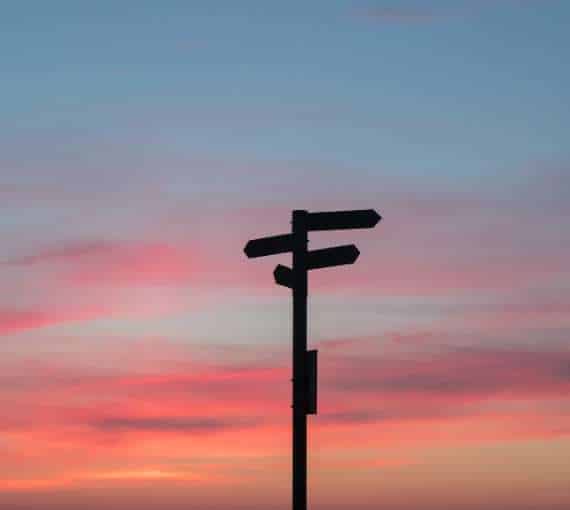 A sign post at sunset with a pink and blue sky
