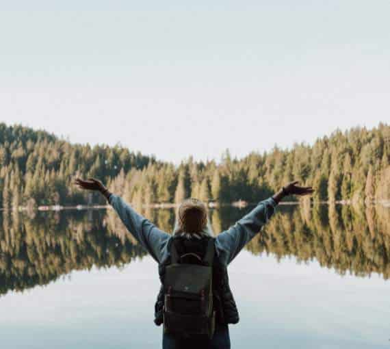 person holding their arms up in front of a lake and forest