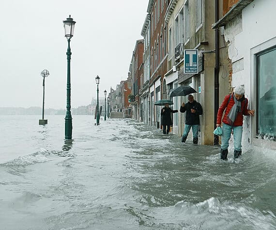 People struggle along a narrow footpath in Venice, up to mid calf in moving water, the morning after the 2019 flood disaster.