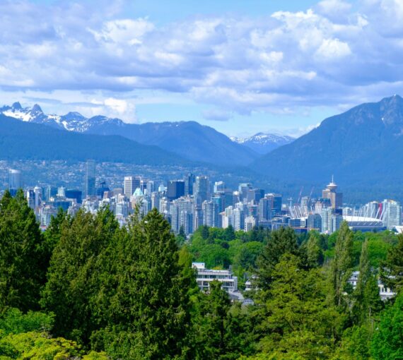 A photo of Vancouver city with mountains behind and trees in the foreground.