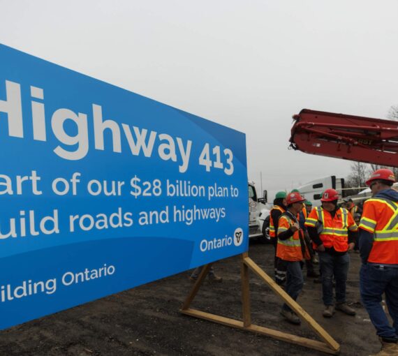 Signage for the highway 413 build with workers in hi-vis vests and hardhats