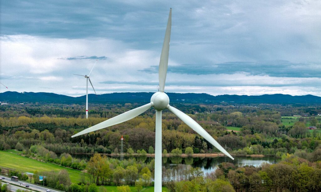 Wind turbines surrounded by greenery, forest, mountains and sky