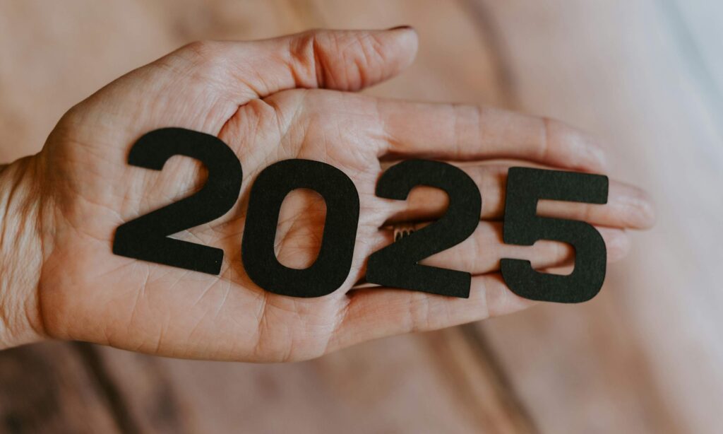 A hand holding the number '2025'