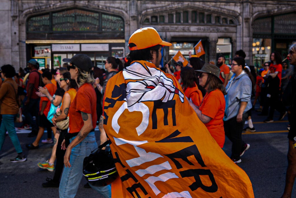 A photo of someone facing a march wearing an orange flag that reads 'every child matters'