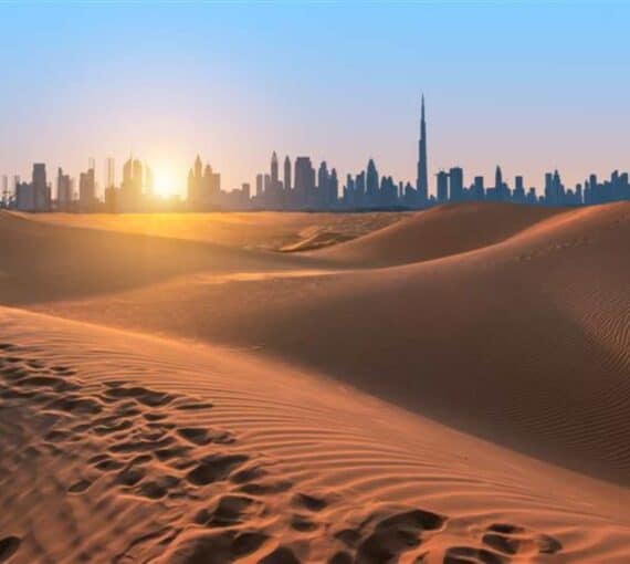 Sand dunes of Dubai, silhouette of Dubai skyline at sunset.