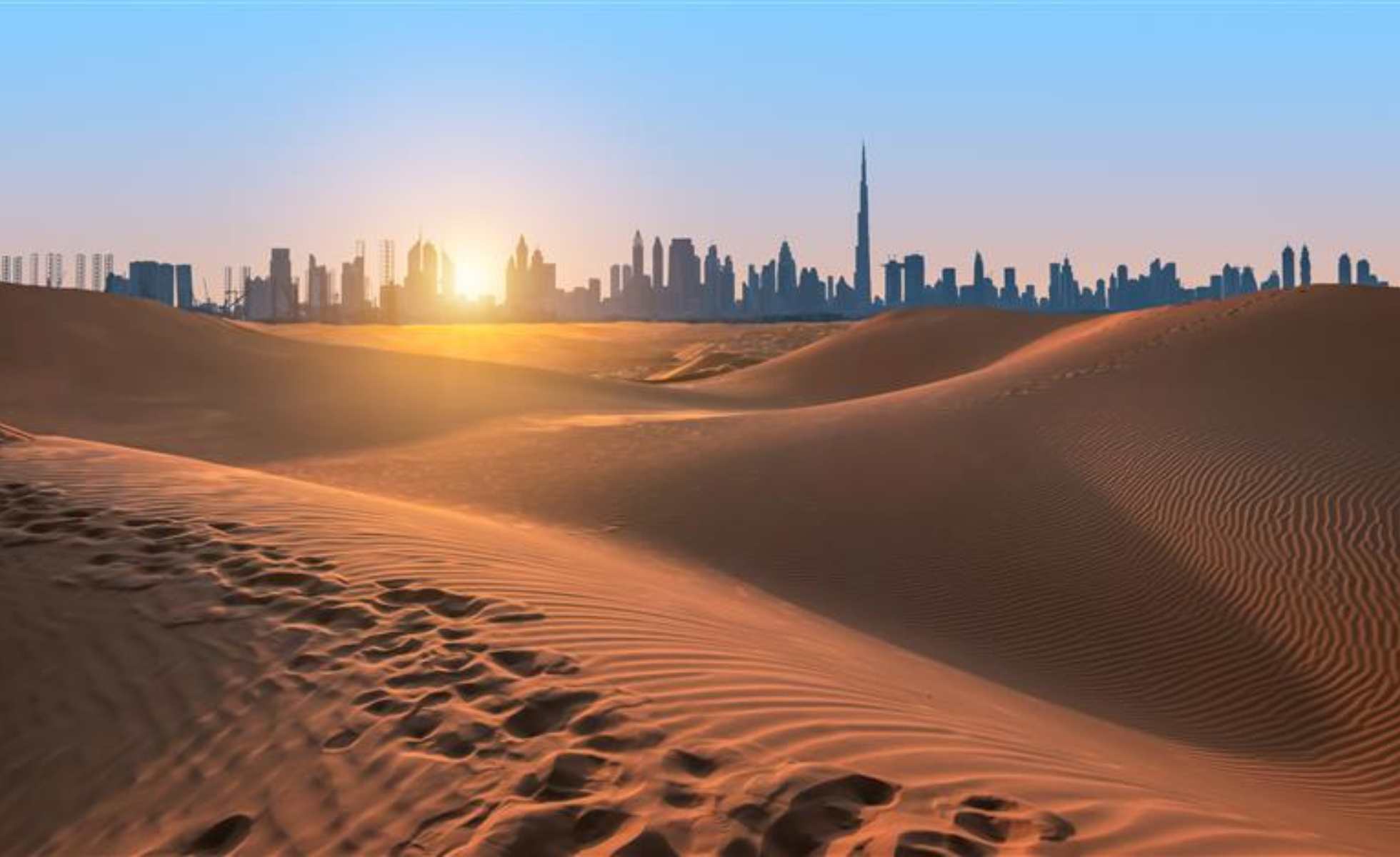 Sand dunes of Dubai, silhouette of Dubai skyline at sunset.