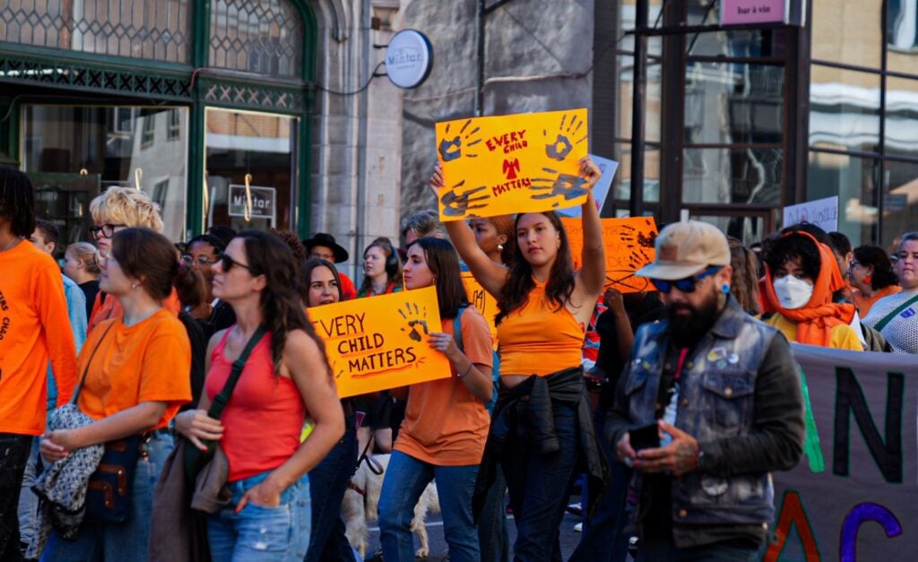 A photo of people marching and holding signs reading 'Every Child Matters'