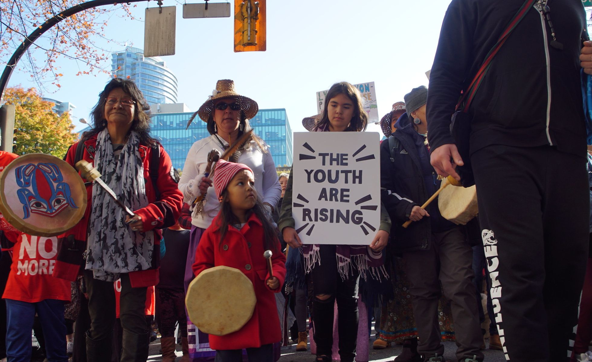 Youth and Indigenous People at a rally holding a sign that reads 'the youth are rising'